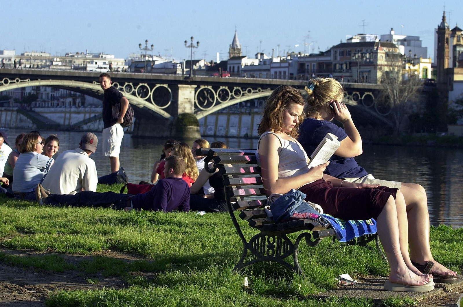 Personas tomando el sol con el puente de Isabel II de fondo