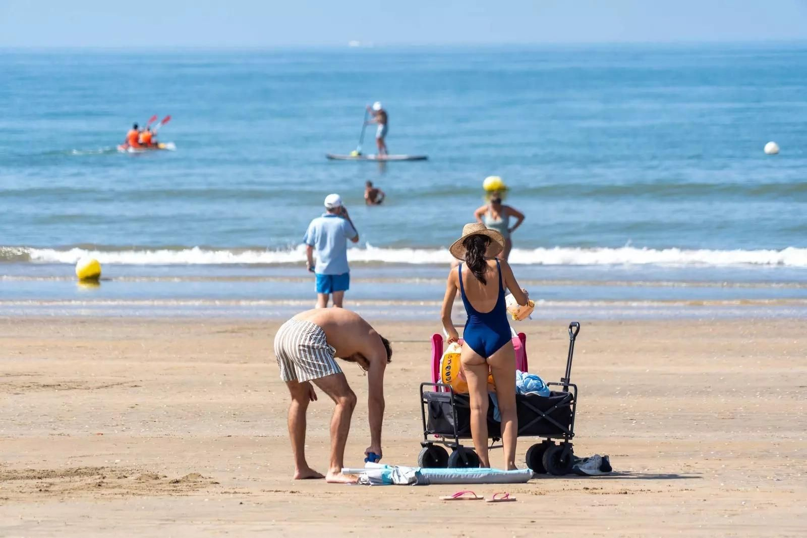 Varias personas despliegan sillas y sombrillas para pasar el día en la playa.