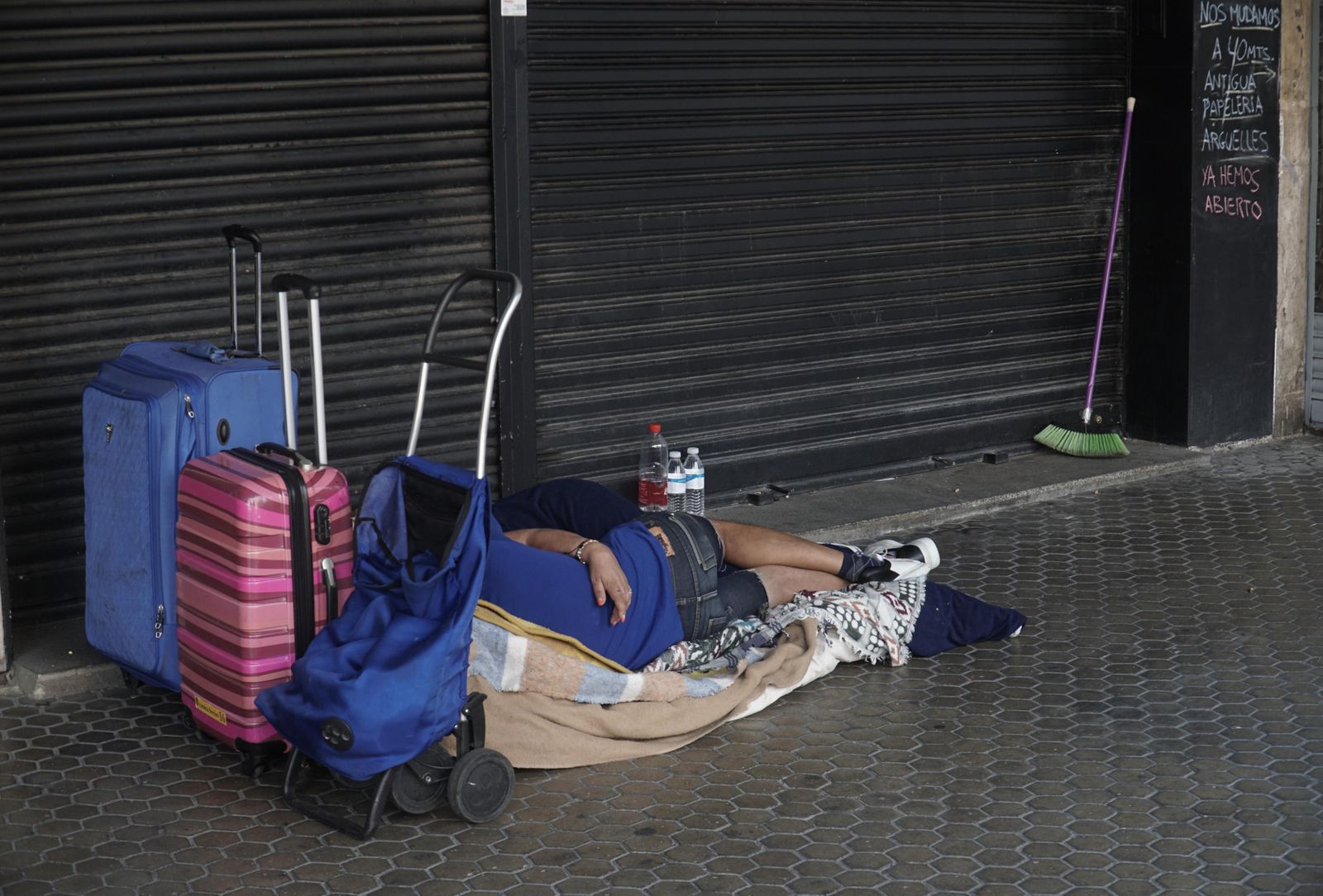 Una persona sin hogar durmiendo en la calle a las puertas de un negocio