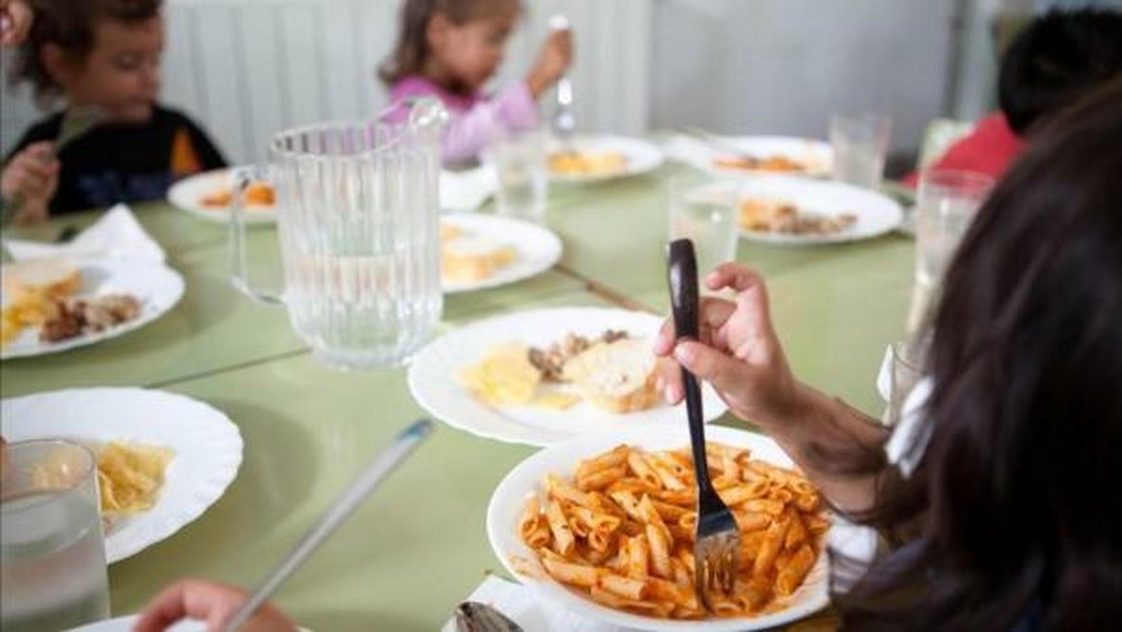 Unos estudiantes comen macarrones con tomate en un comedor escolar.