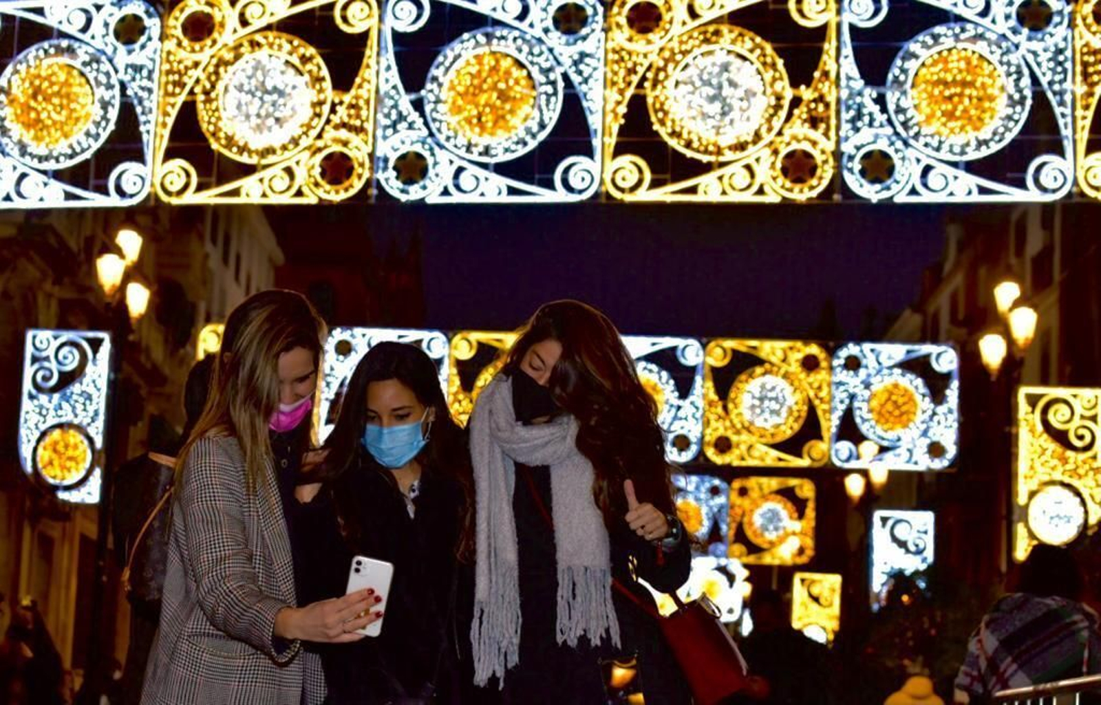 Tres jóvenes se hacen un 'selfie' bajo el alumbrado de la Avenida de la Constitución.
