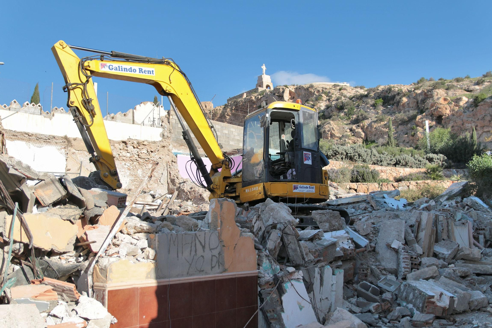 La retroexcavadora en la calle Hércules con el Sagrado Corazón de Jesús al fondo