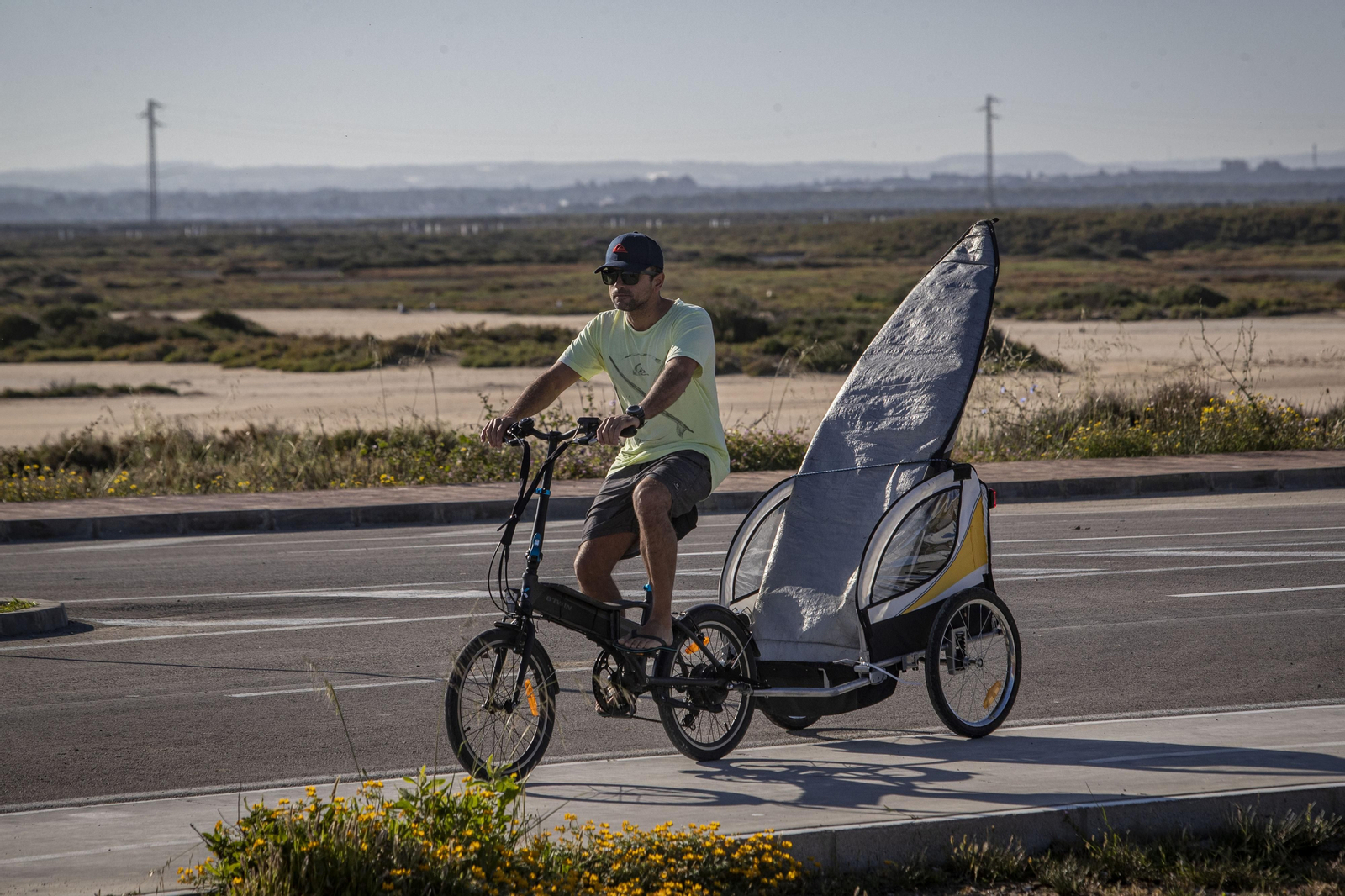 Un surfero en bici y con la tabla en un remolque en los accesos de la playa de Camposoto durante el estado de alarma.