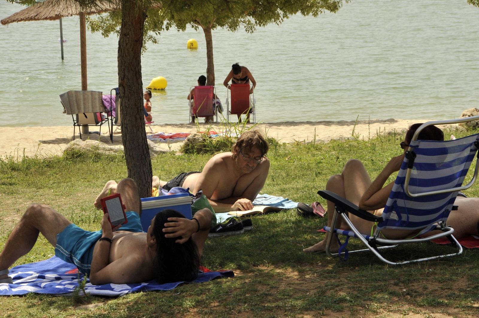 Un grupo de personas disfruta de una jornada de descanso en la playa artificial habilitada en el lago de Arcos.