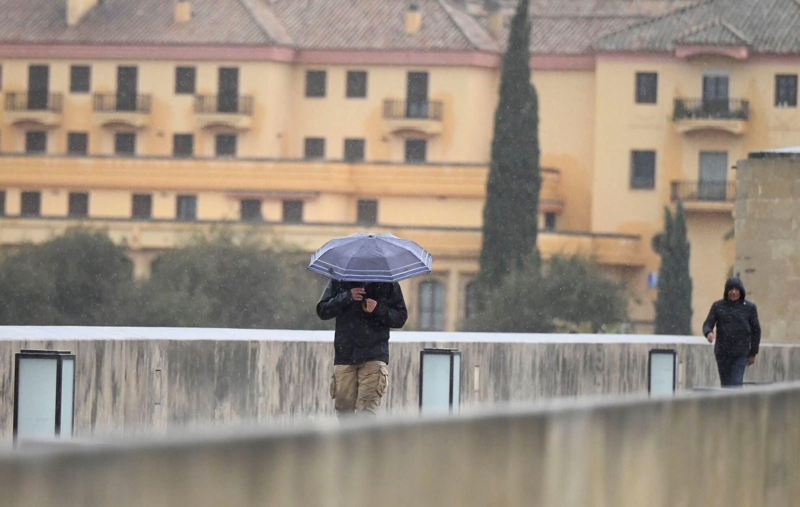 Una persona se protege de la lluvia bajo un paraguas a su paso por el Puente Romano