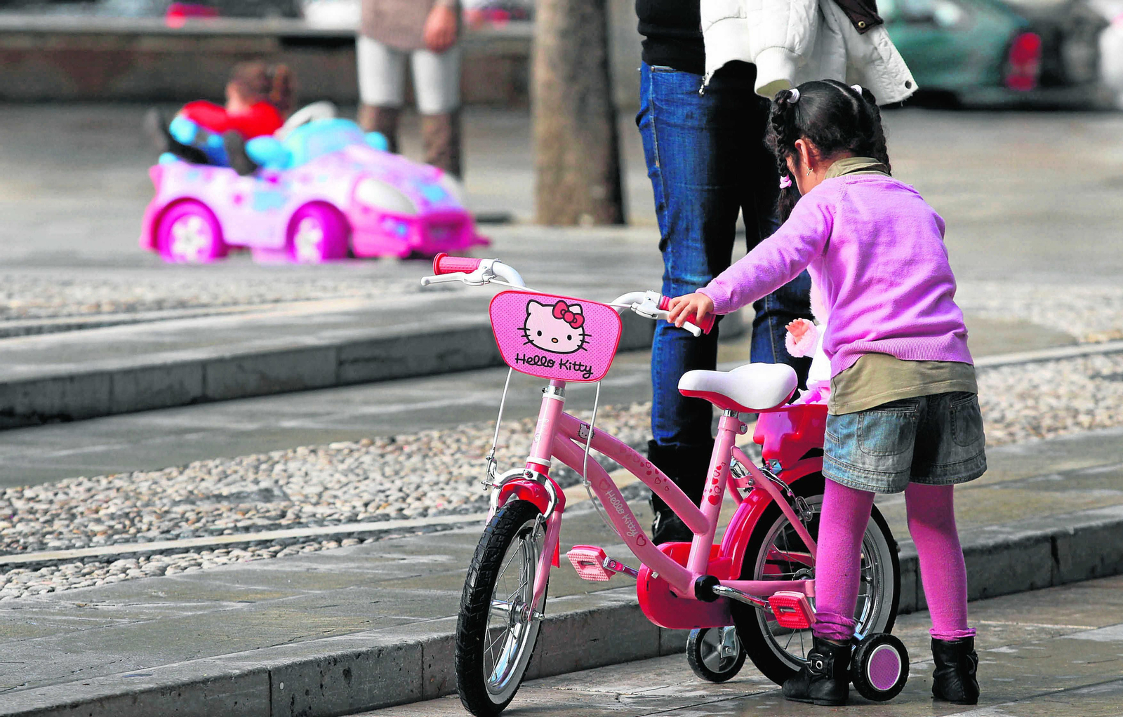 Una niña  juega con su bicicleta en un parque, vigilada por su madre.