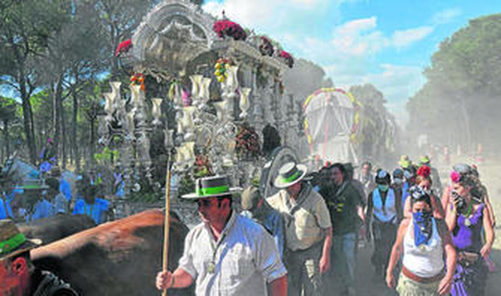 La carreta del simpecado de Triana avanza por la Raya Real rodeada de peregrinos y envuelta en una nube de polvo.