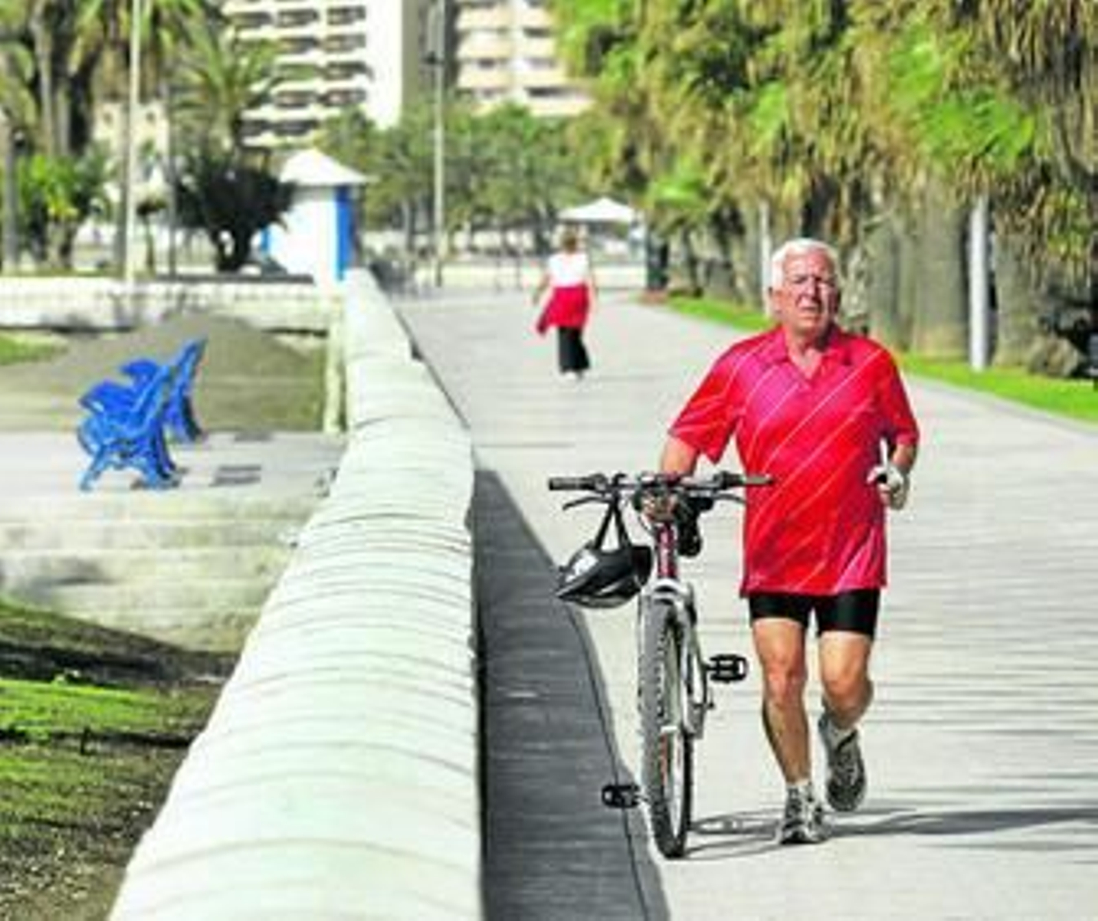 Un ciclista, a pie, por el paseo marítimo Pablo Ruiz Picasso.
