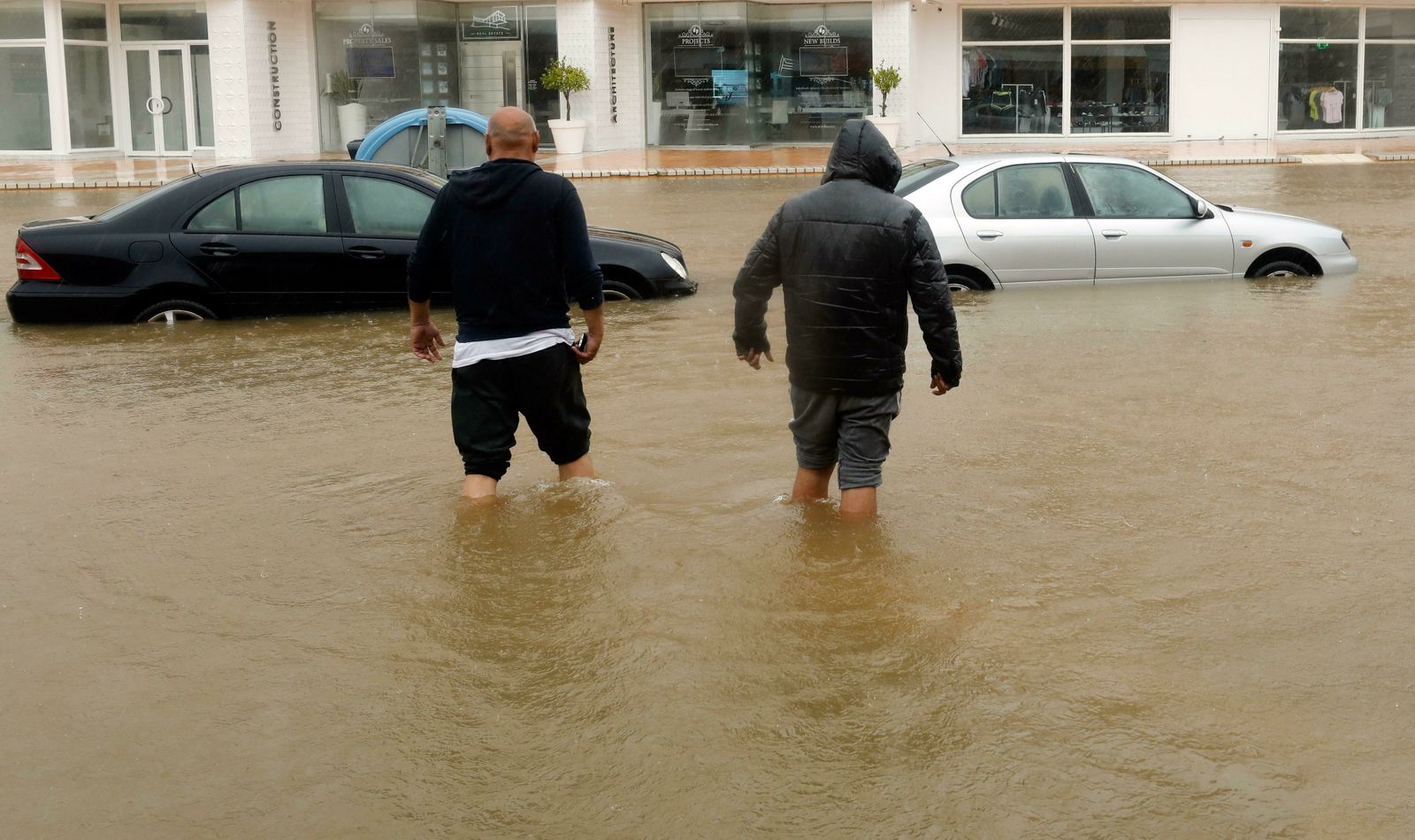 Dos hombres caminan con agua hasta las rodillas por una calle de Jávea (Alicante).