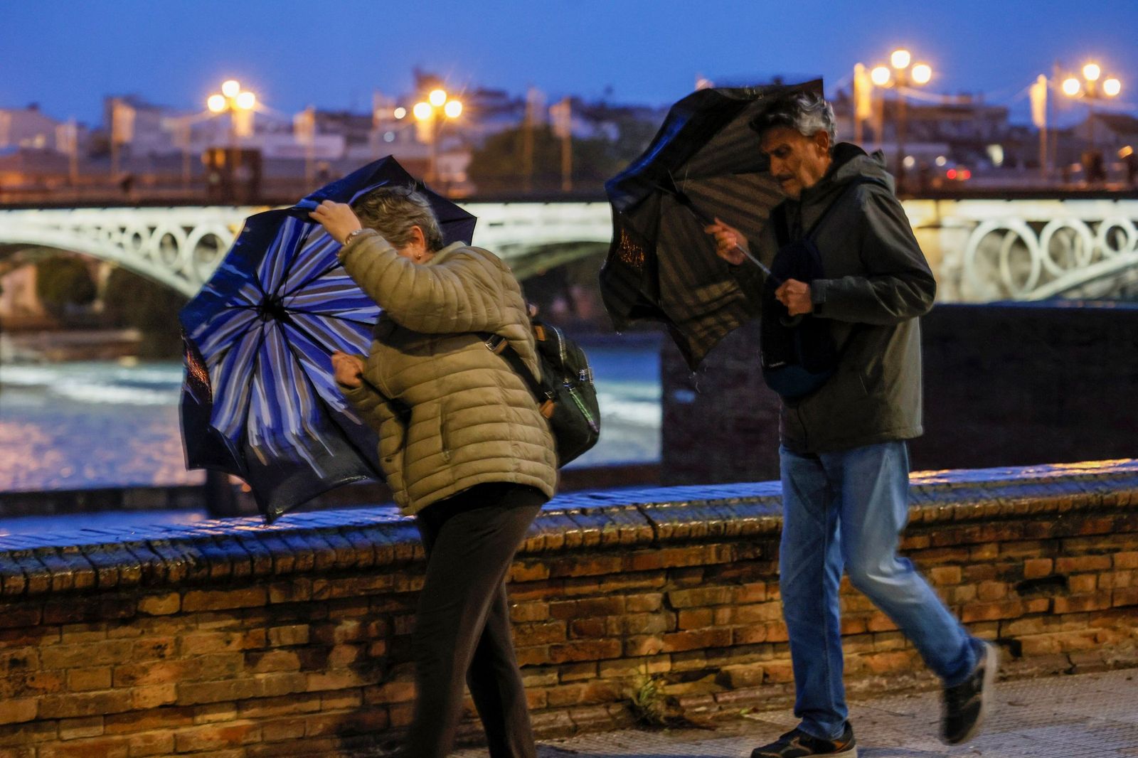 Dos personas intentan protegerse de la lluvia mientras luchan contra el viento.