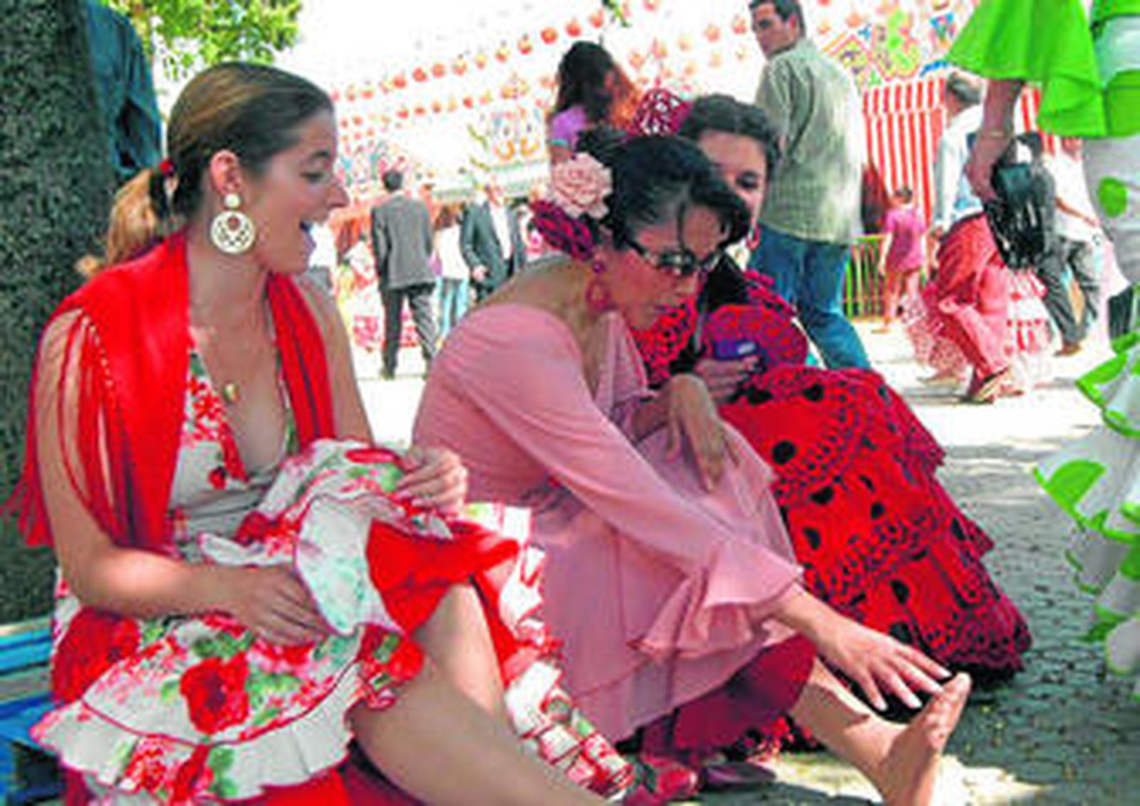 Tres mujeres vestidas de flamenca descansan durante una jornada de feria.