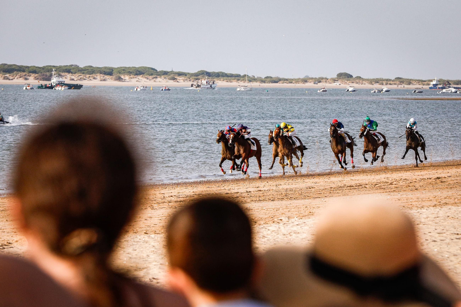 Siete caballos se disputan la segunda carrera de la tarde, el premio Distribuciones Cuevas, en la playa de Las Piletas de Sanlúcar con Doñana al fondo.
