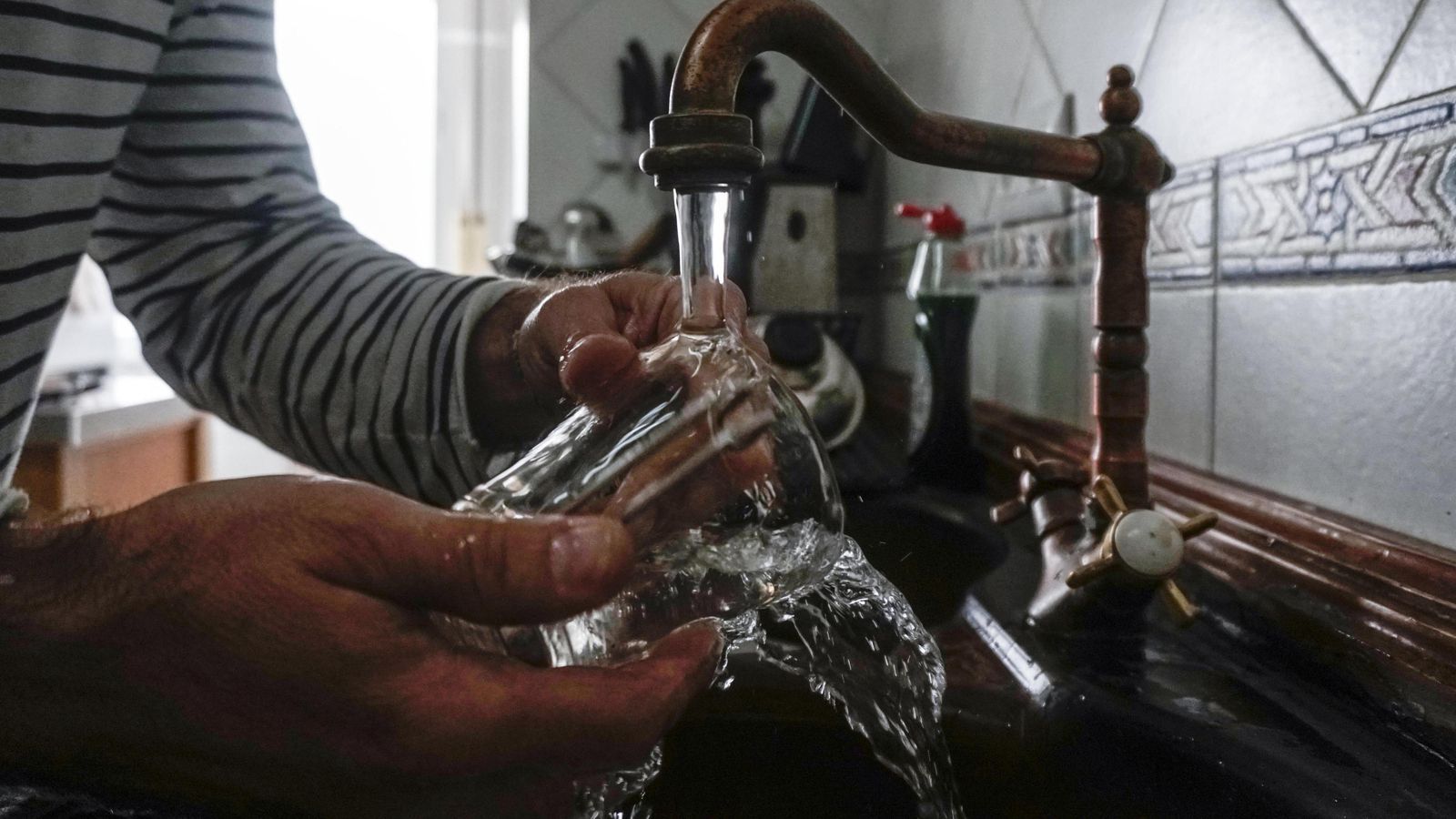Un cliente de Emasesa lava un vaso de cristal en un grifo de la cocina.