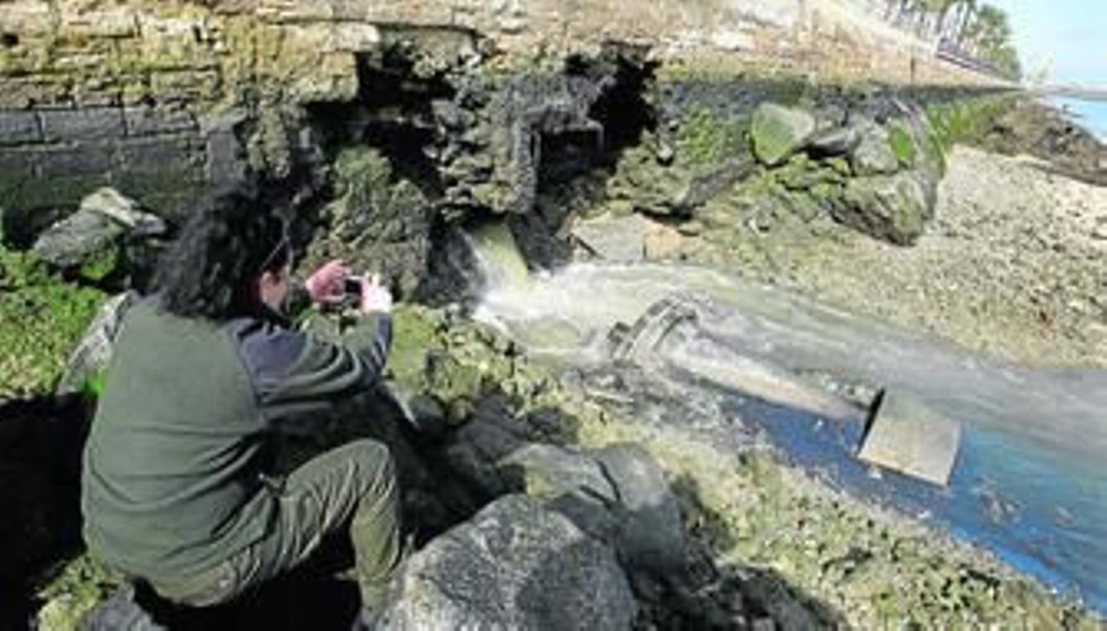 Una de las agentes de Medio Ambiente fotografía el caño de agua que salía ayer del aliviadero de la Barriada de la Paz para redactar el posterior informe.