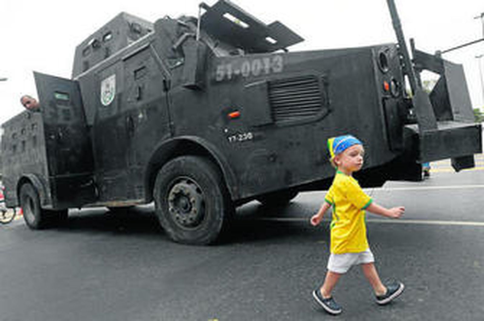 Un niño ataviado con la camiseta de Brasil pasa por delante de un vehículo blindado de la Policía.