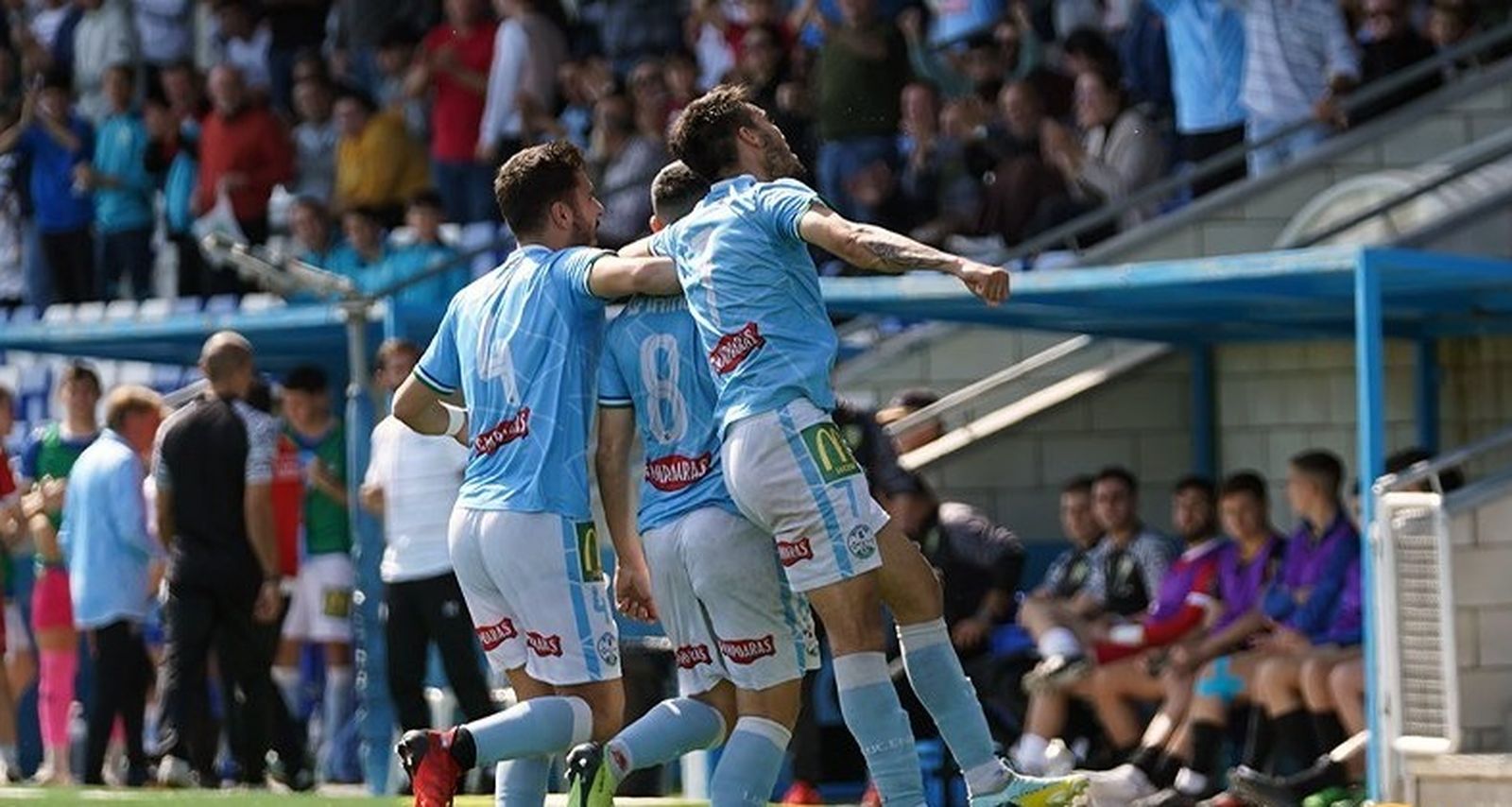 Los jugadores locales celebran el gol ante los rostros serios del banquillo conileño.