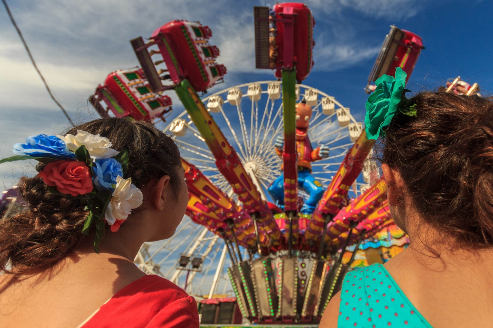 Unas niñas miran hacia una de las atracciones clásicas de la Feria portuense.