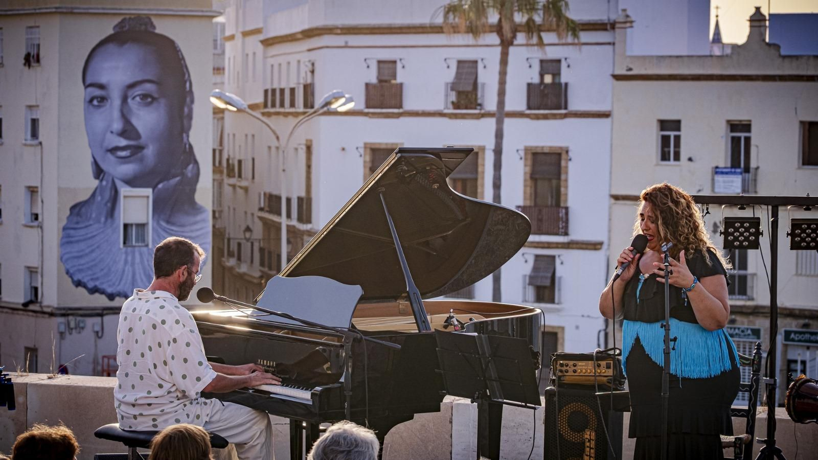 Un momento de la actuación de Leo Power, con Javier Galiana al piano, en el paseo superior de la Puerta de Tierra, ante el mural en homenaje a la cantaora, leyenda del flamenco de Cádiz.