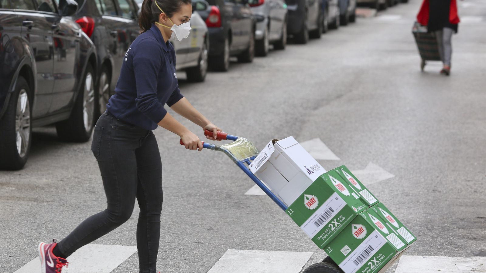 Una mujer lleva un carro con varias cajas de productos de limpieza.