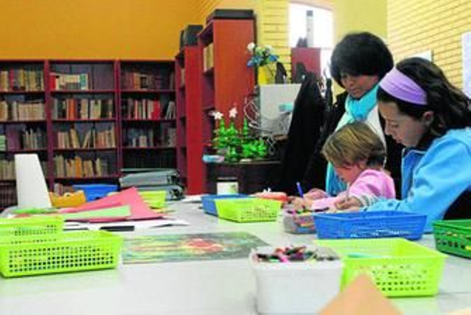 Dos niñas se entretienen dibujando ante la mirada de la monitora en la ludoteca.