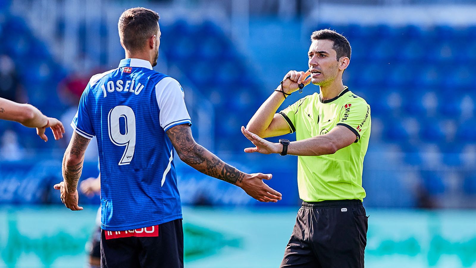 El joven árbitro gallego atiende al pinganillo mientras hace una indicación al alavesista Joselu.