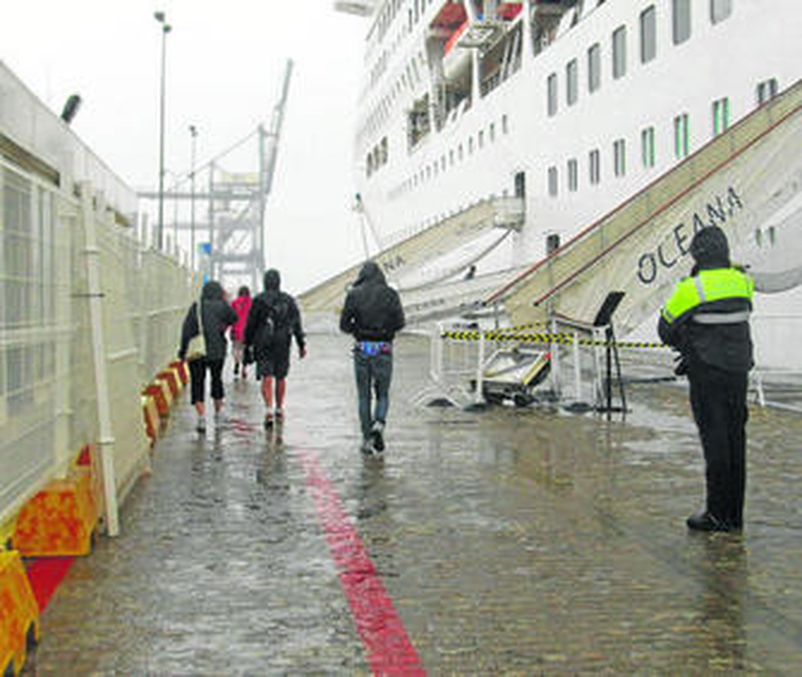 Policía portuario y cruceristas, mojándose bajo la lluvia, a pocos metros de la terminal, que ayer estaba cerrada.