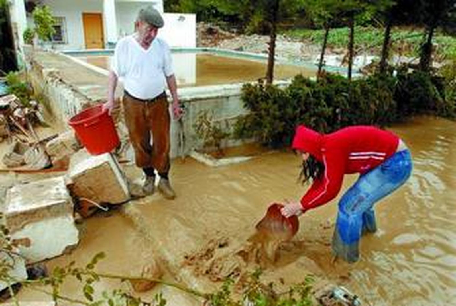 Una joven achica agua en su vivienda en Puentes de la Sierra (Jaén), una de las zonas más afectadas por la tromba de agua, junto a su abuelo.