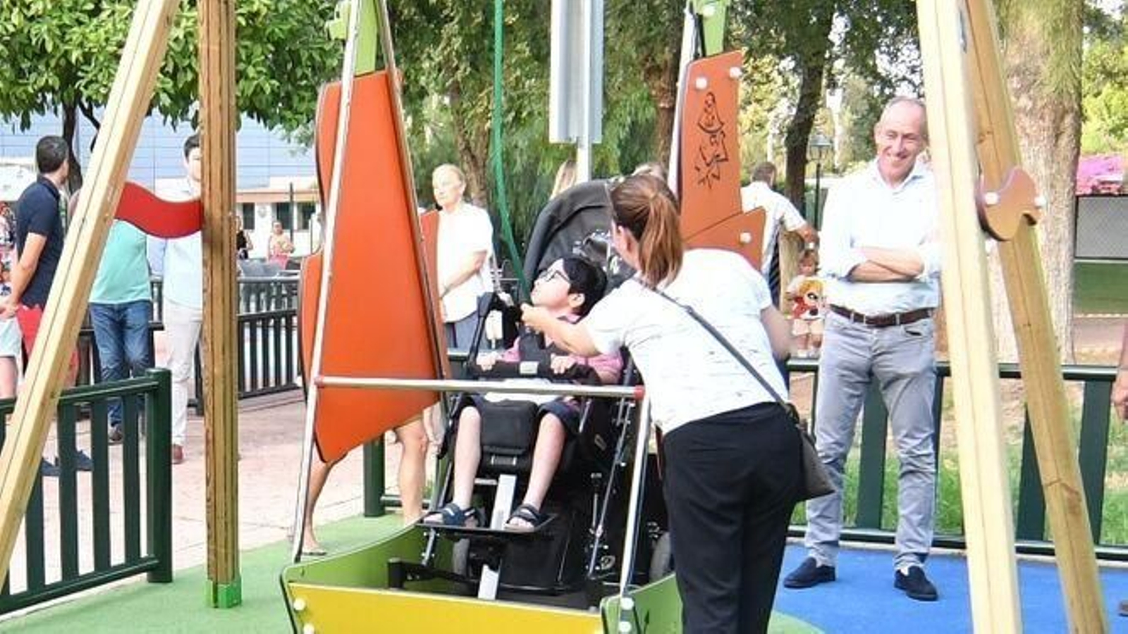 El primer pequeño en disfrutar del nuevo columpio adaptado para sillas de ruedas junto a su madre y el alcalde de Tomares, José María Soriano, al fondo.