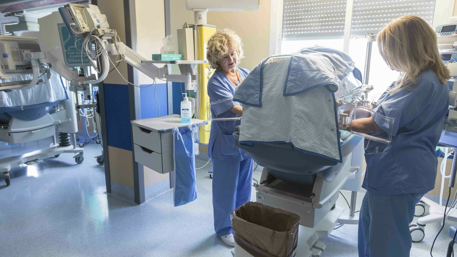 Dos trabajadoras de la Unidad de Neonatología atienden a un prematuro en su incubadora.