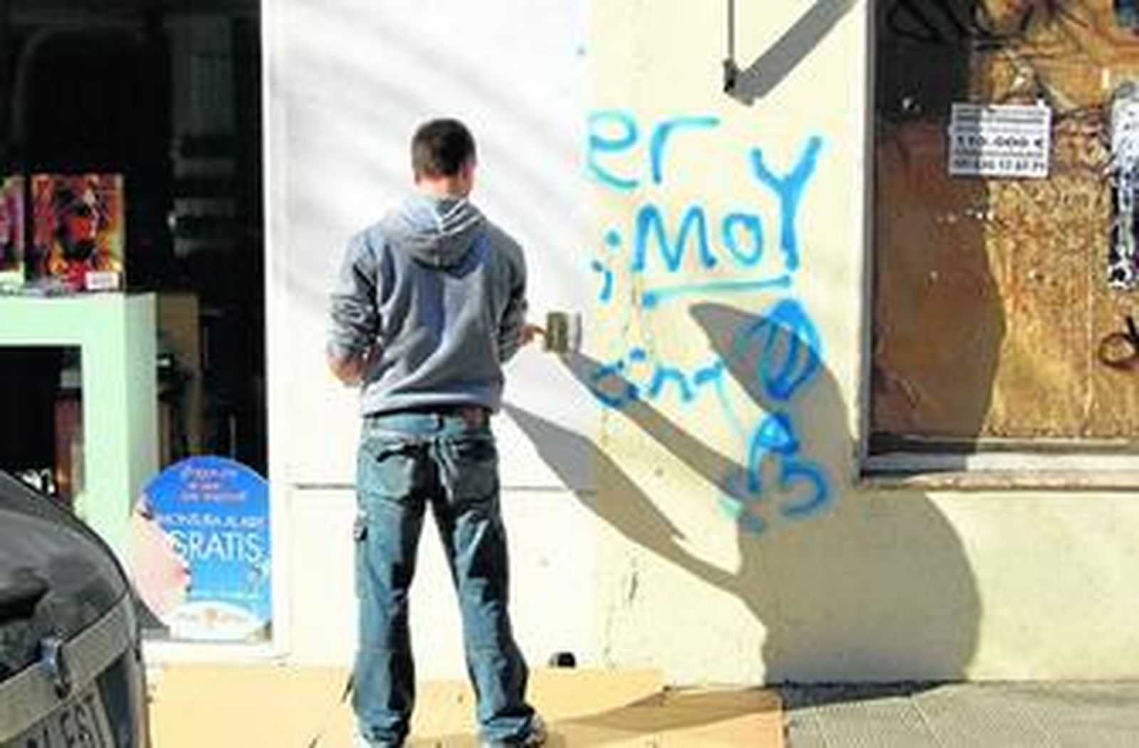 Un joven borra pintadas de una fachada del municipio.