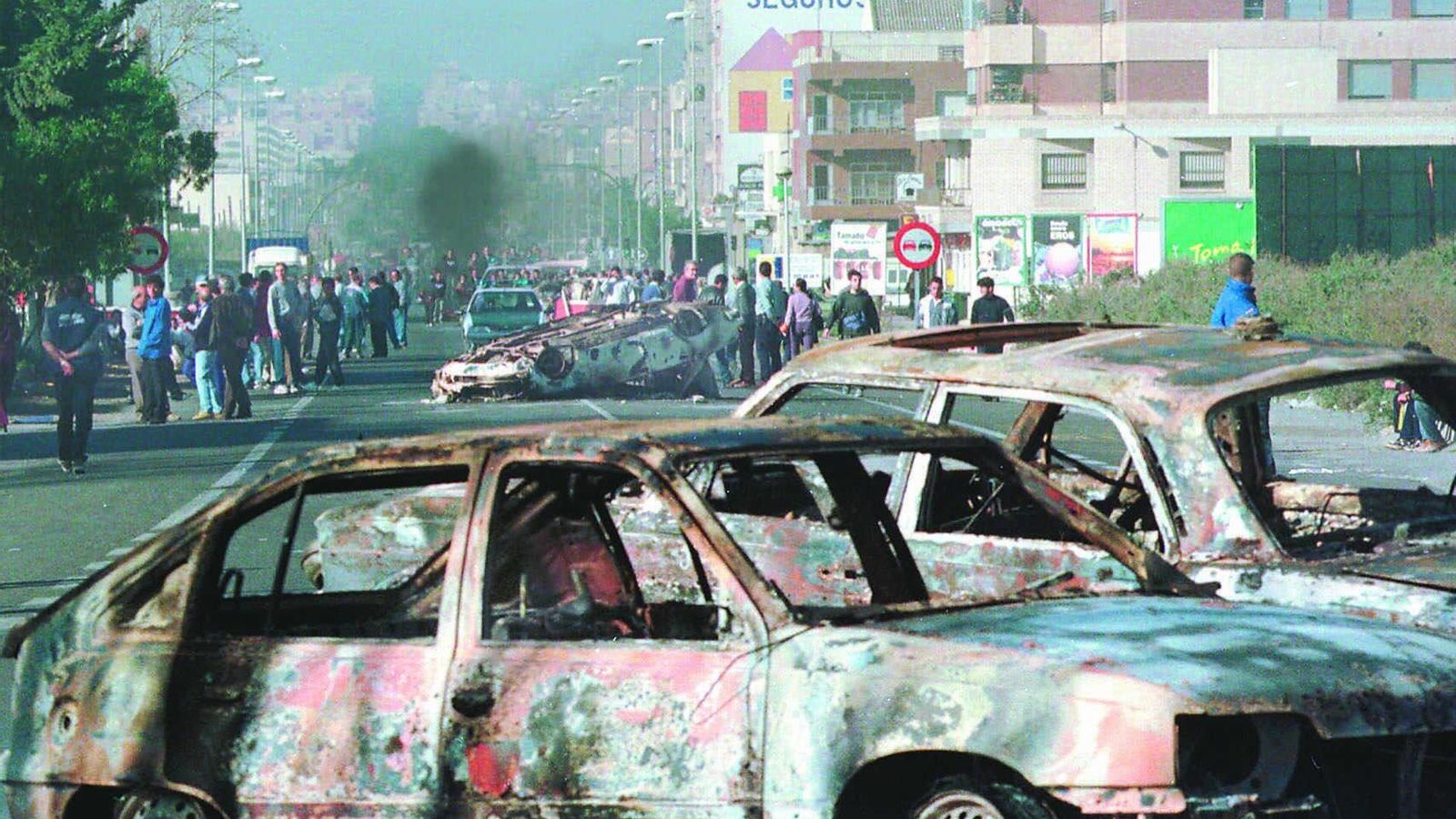 La calles de acceso a Santa María del Águila con varios coches quemados.