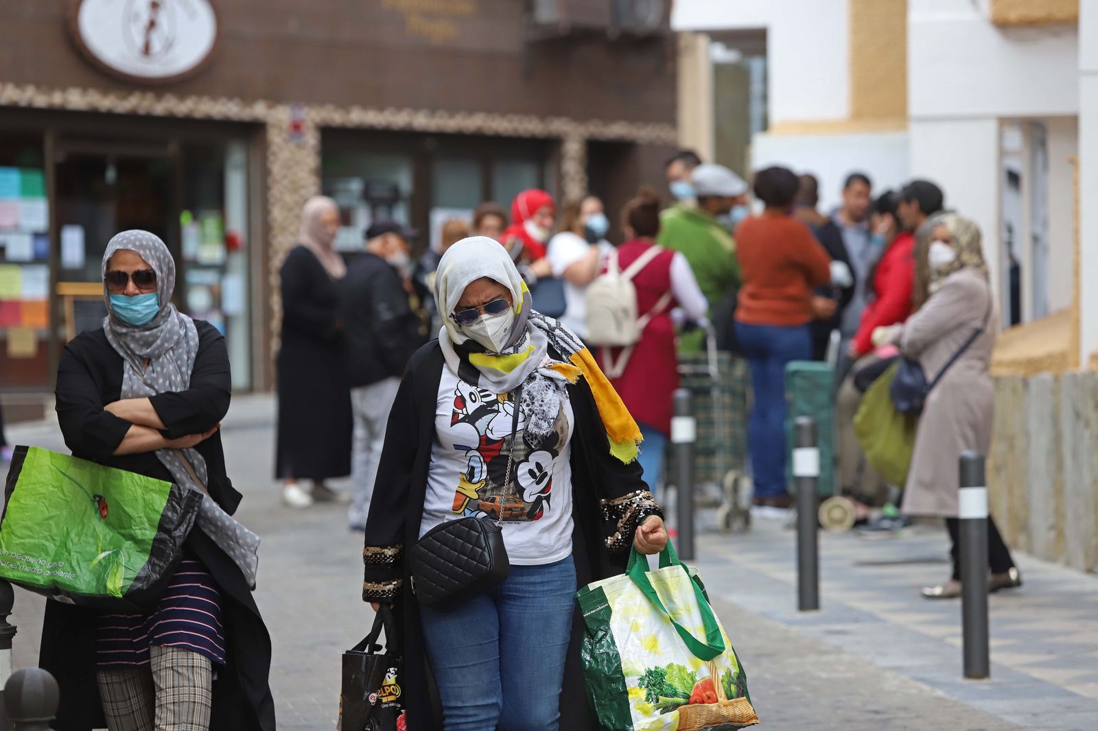 Dos mujeres cargan con la bolsa de donativos de Cáritas y, al fondo, el resto de personas que aguardan su turno en La Palma.