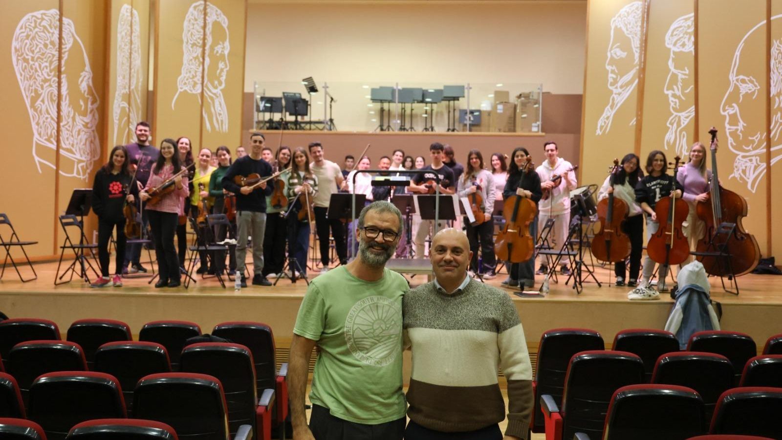 El director del proyecto junto al director del conservatorio, delante de la formación musical.