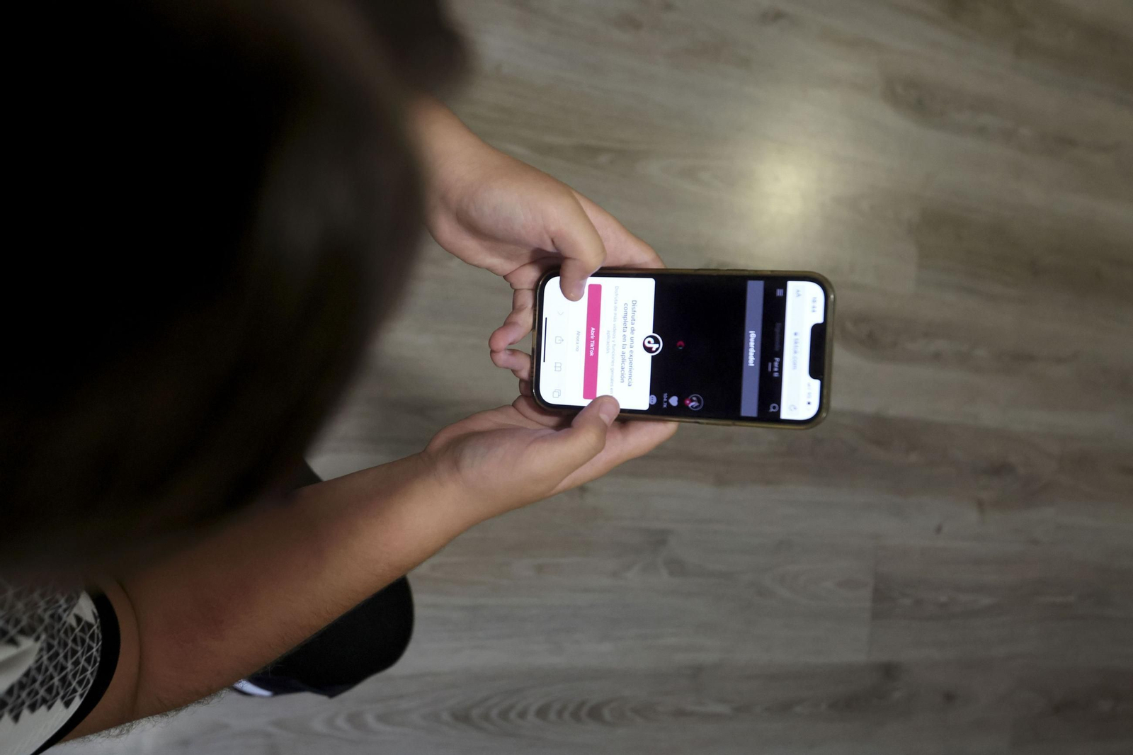 Una mujer consulta su teléfono móvil, sujetándolo con sus dos manos, en su casa para visualizar un vídeo en una red social. Una mujer consulta su teléfono móvil, sujetándolo con sus dos manos, en su casa para visualizar un vídeo en una red social.