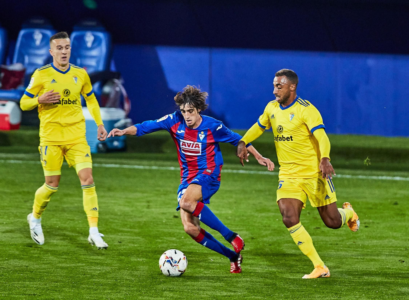 Bryan Gil trata de escaparse de Akapo ante la mirada de Salvi, en el Eibar-Cádiz.