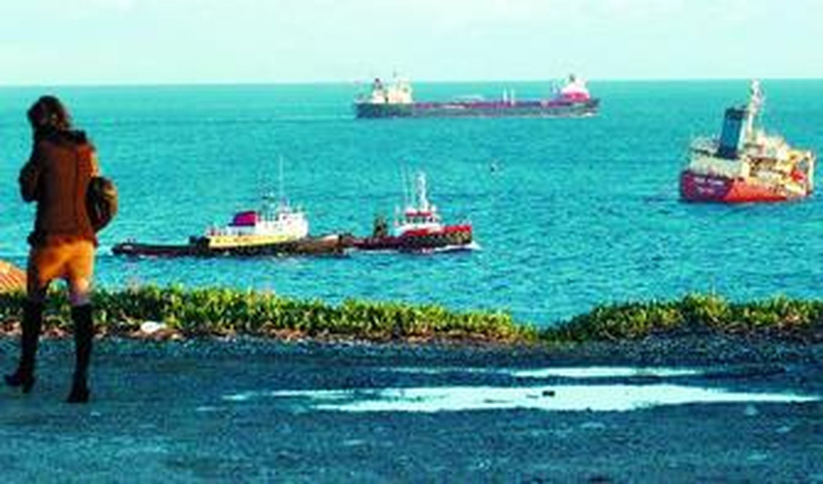 Una mujer observa desde la costa las tareas de desmontaje del chatarrero 'New Flame', a la derecha de la imagen.