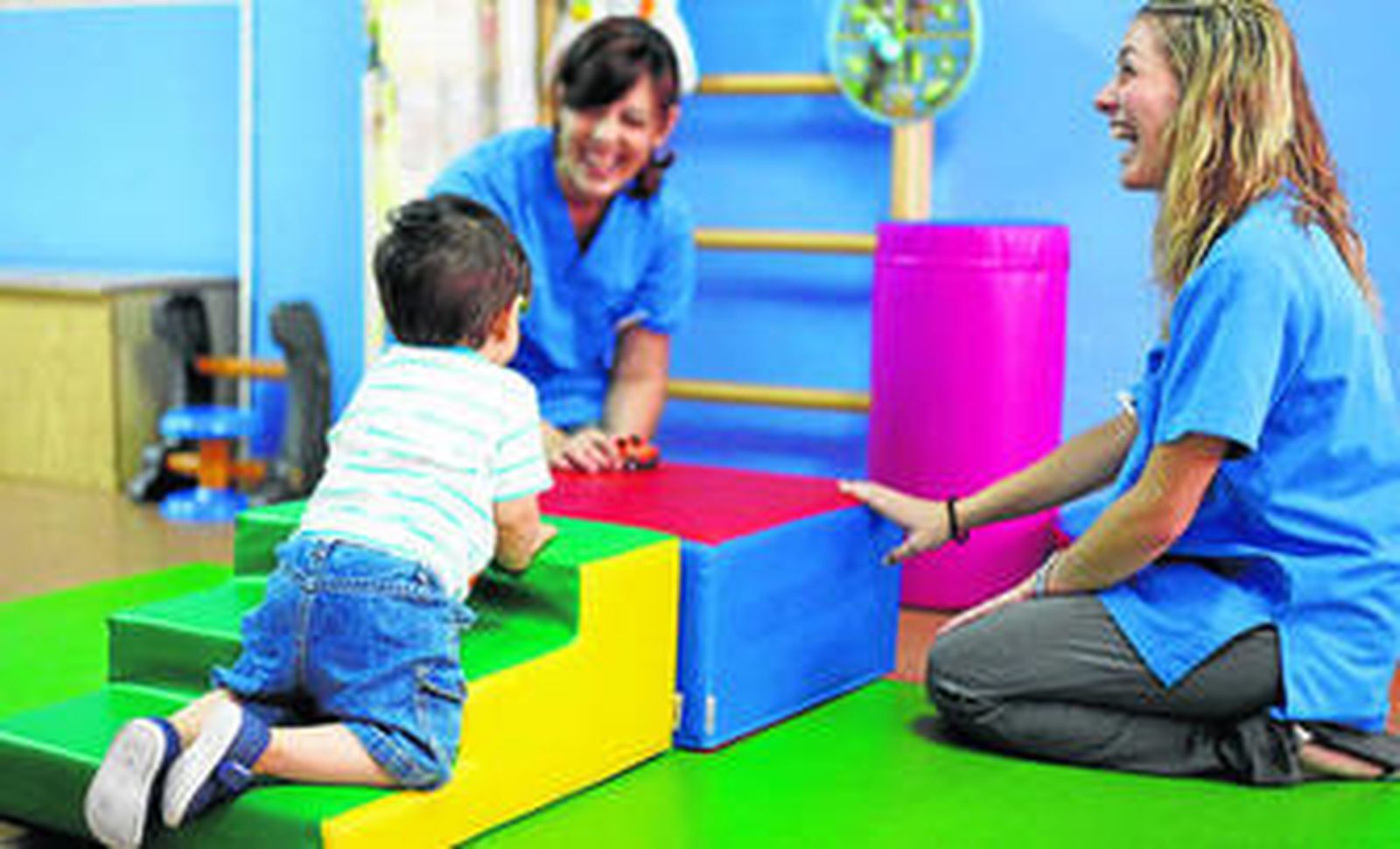Dos fisioterapeutas realizan ejercicios de motricidad con un pequeño en un Centro de Atención Temprana.