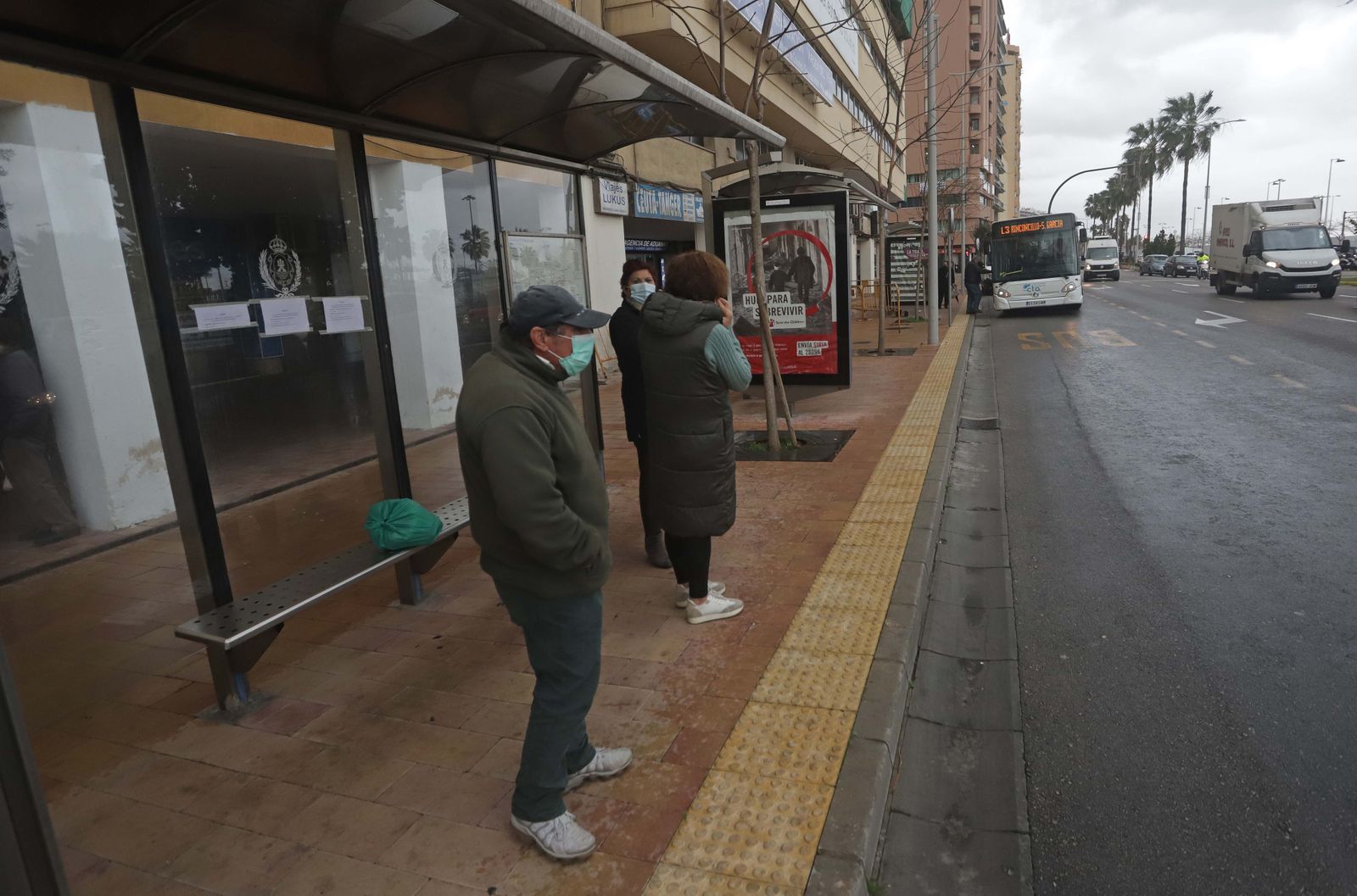 Varias personas esperan a que llegue el autobús en La Marina.