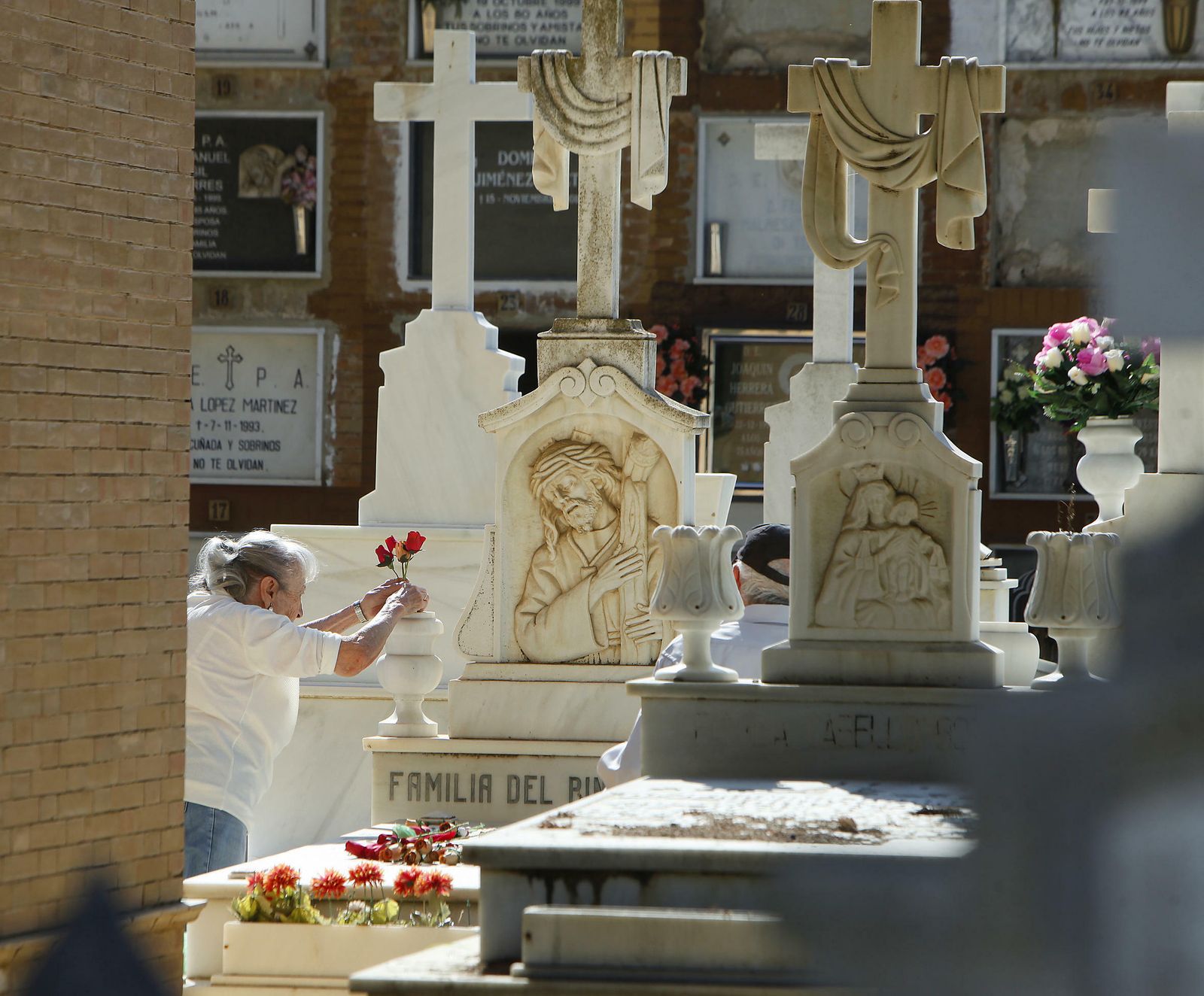 Una mujer deposita flores sobre la tumba de un ser querido en el cementerio de Sevilla.
