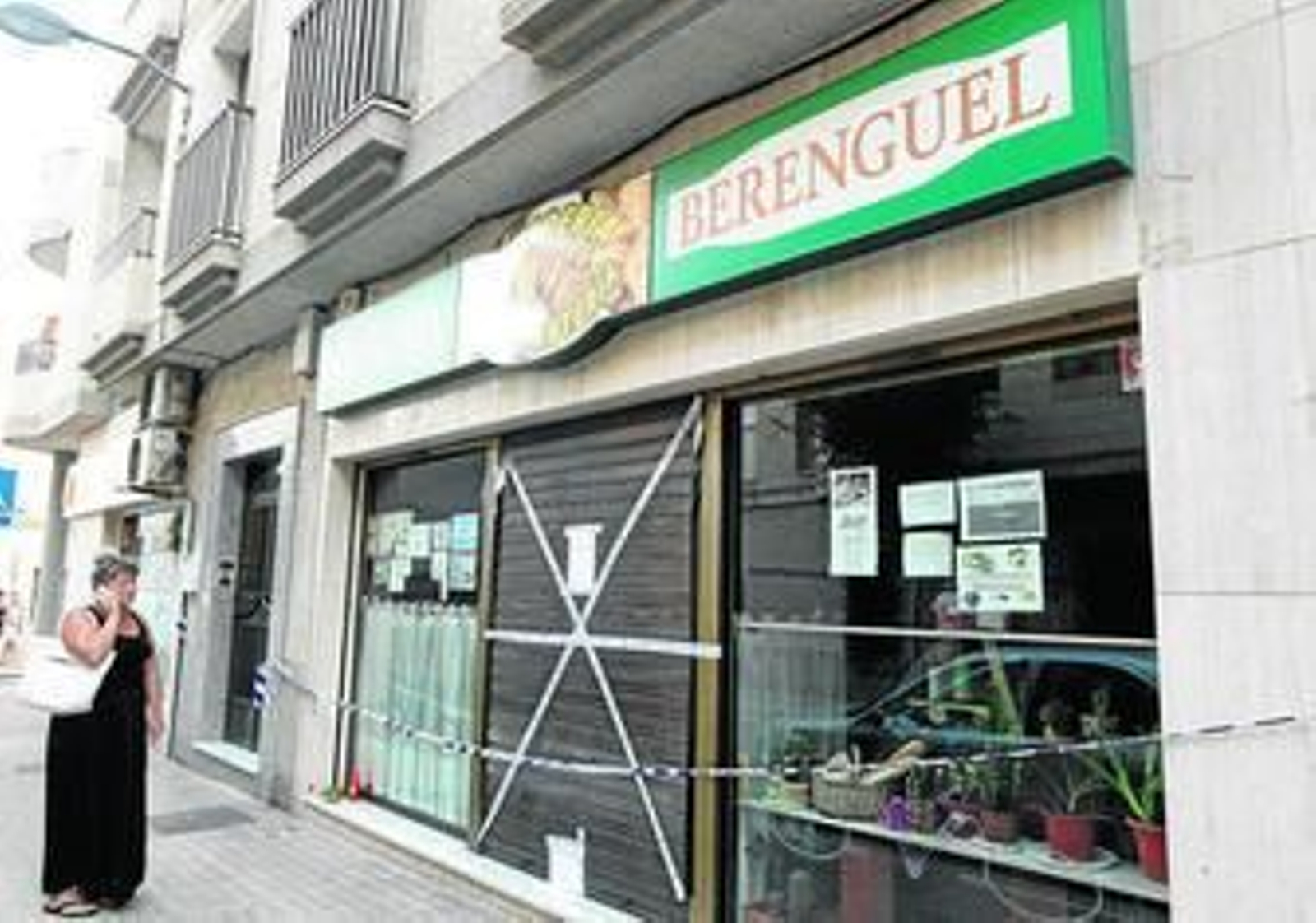 Una mujer se para ante la puerta del establecimiento precintado. Una vela y una flor recuerdan a la fallecida.