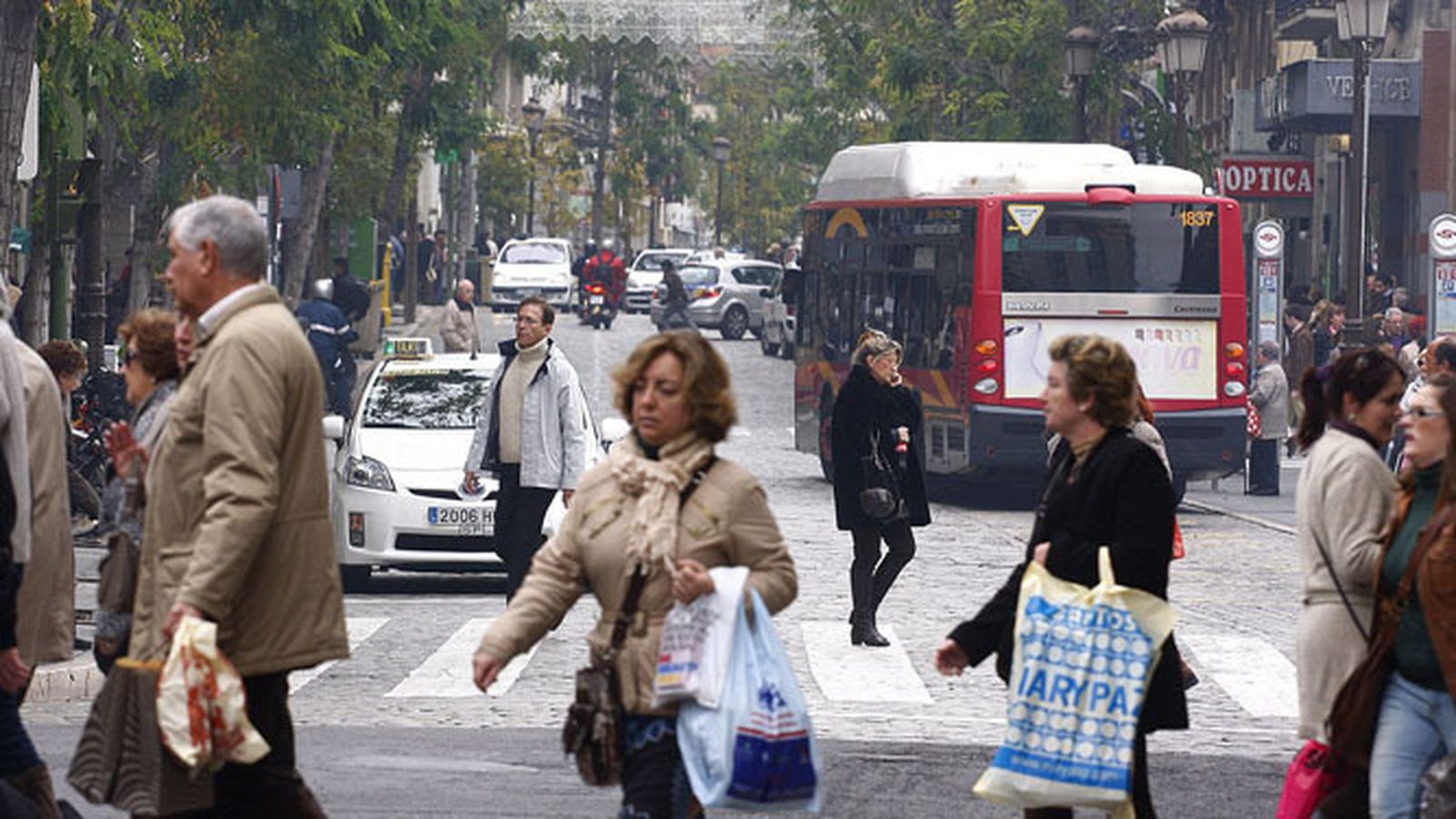 Un autobús de Tussam en una parada en La Campana con varios viandantes por la carretera.