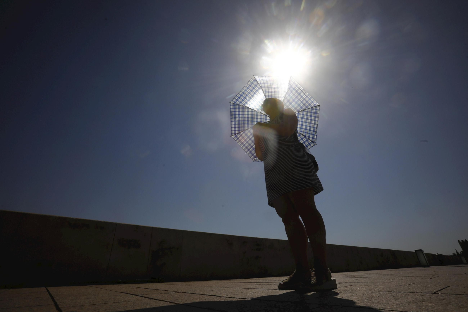 Una mujer se protege del sol con un paraguas a su paso por el Puente Romano Una mujer se protege del sol con un paraguas a su paso por el Puente Romano