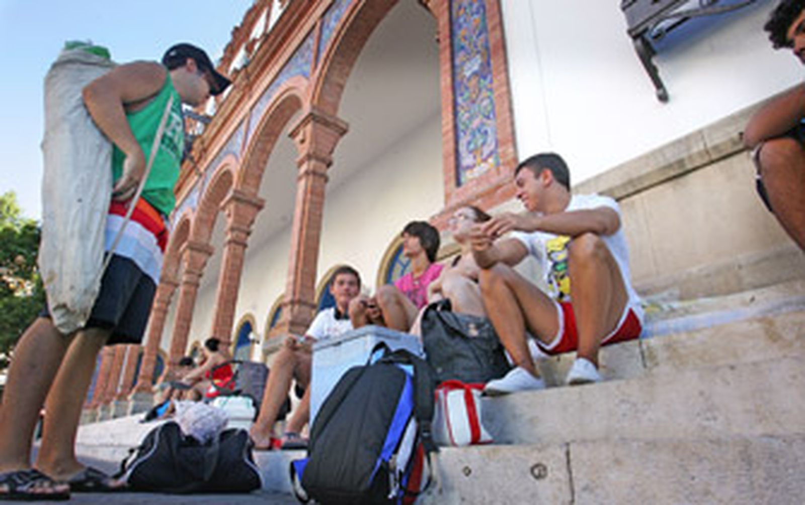 Un grupo de amigos espera, ayer, en los escalones de la estación de trenes con todo lo necesario para irse a la playa./Pascual