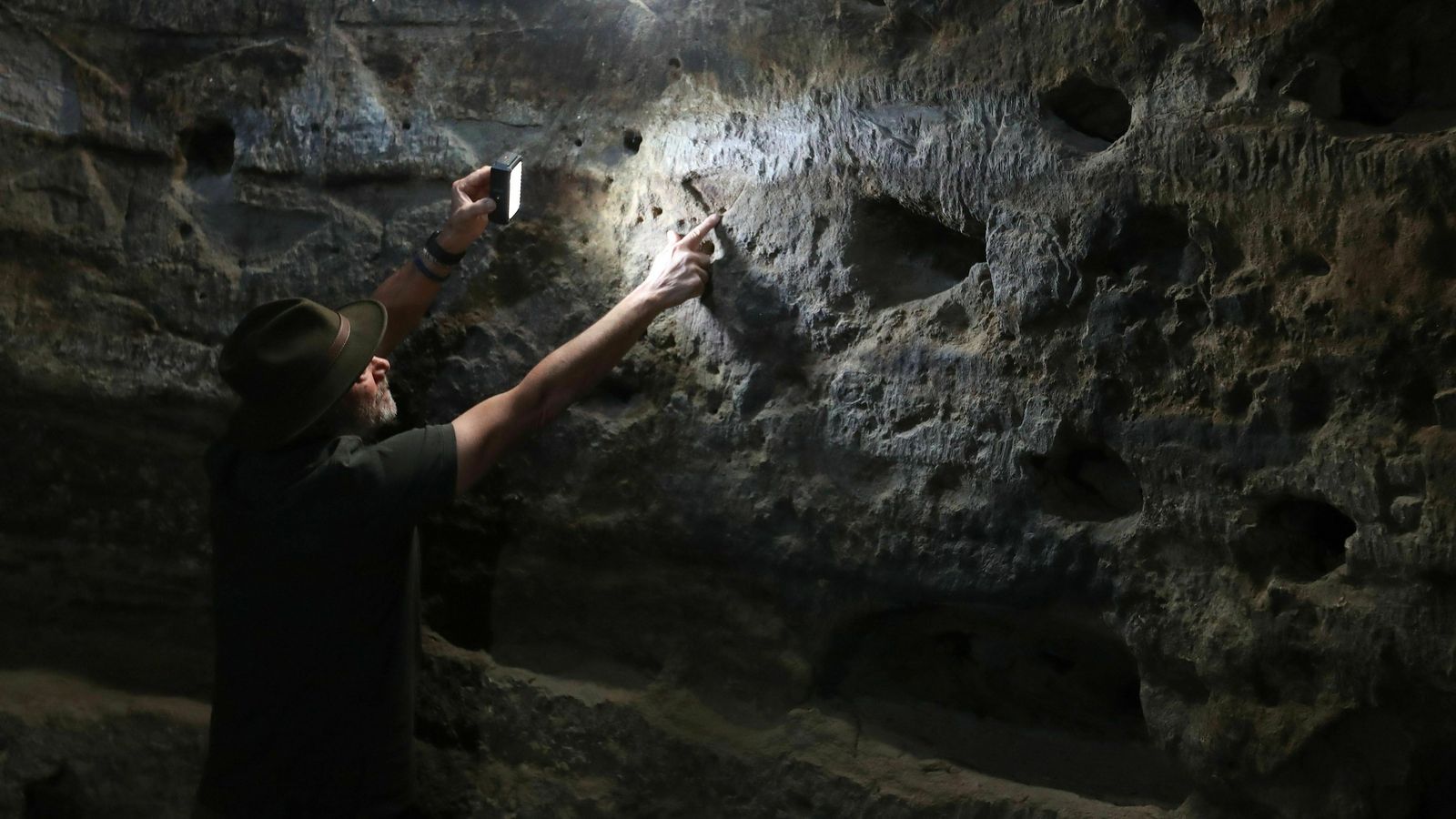 El arqueólogo Julio Cuenca señala los grabados con forma de triángulo público que la luz del amanecer va recorriendo en el interior de la cueva desde el equinoccio de primavera hasta el de otoño.