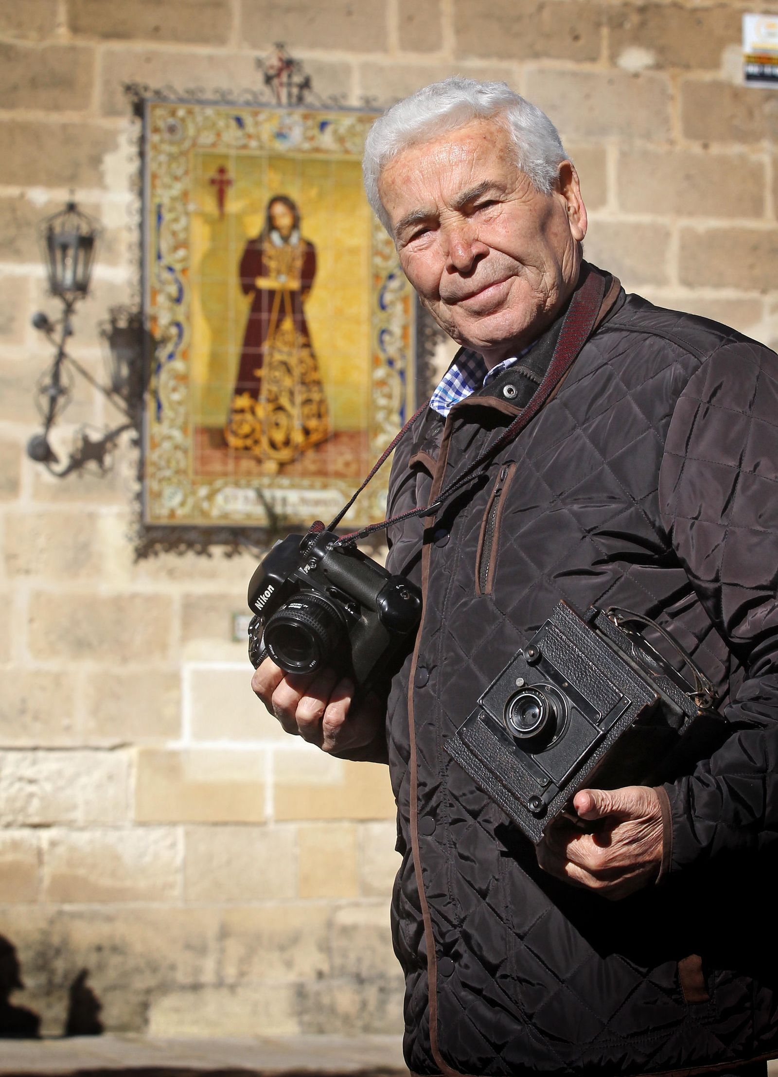 Iglesias posa con dos cámaras analógicas con las que trabajó, delante del azulejo de Jesús del Prendimiento.