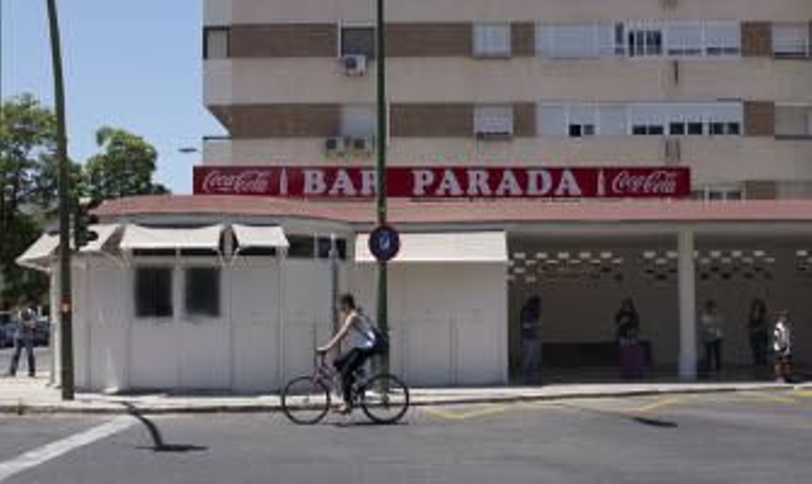 Una joven pasa montada en bicicleta junto a la fachada del Bar Parada, en la glorieta de Heliópolis. / Juan Carlos Vázquez