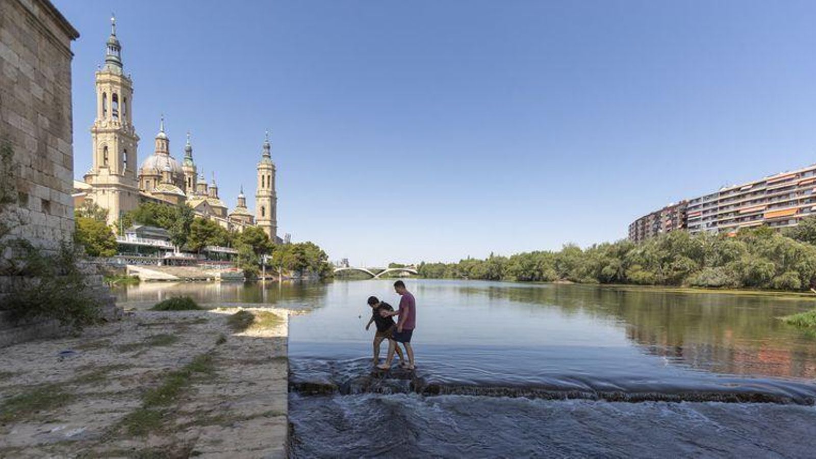 Dos personas cruzan el Ebro andando a su paso por Zaragoza