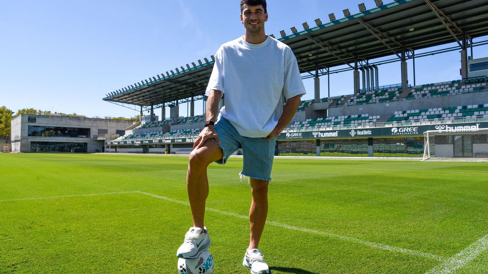 Marc Roca sonríe mientras posa con la grada principal al fondo en la ciudad deportiva.