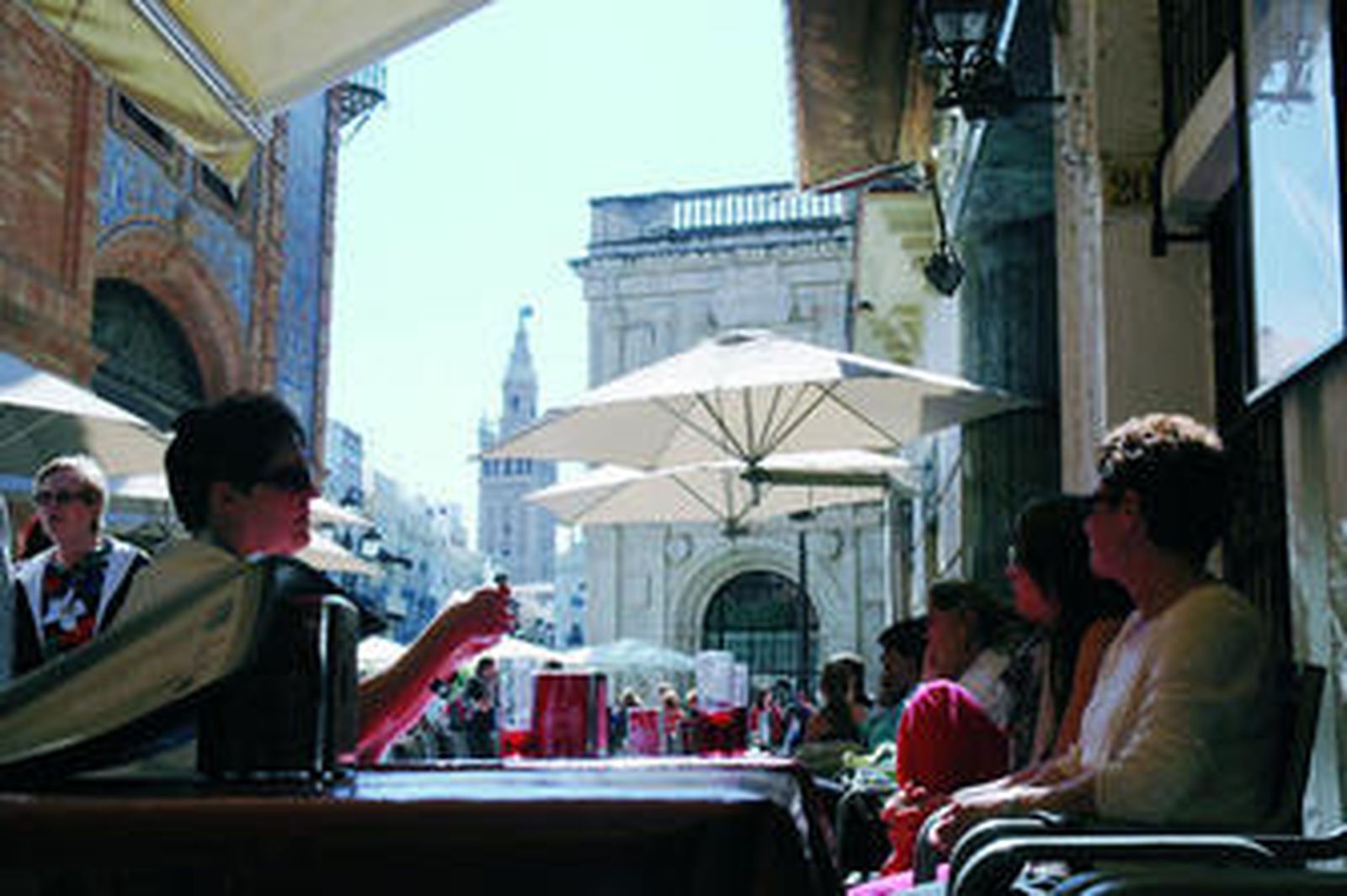 Clientes de una terraza del entorno de la Plaza de San Francisco, con la Giralda al fondo.
