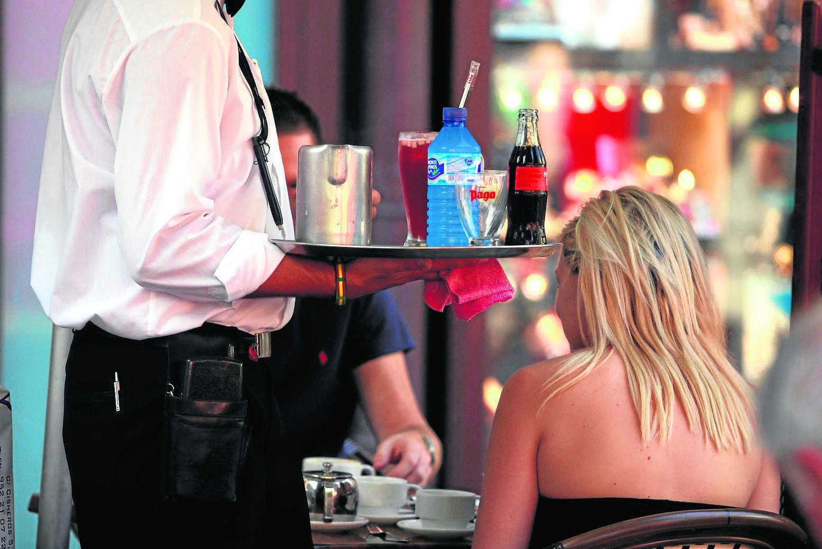 Un camarero atiende a dos personas en los veladores de un bar.